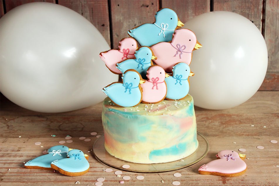 Gender Reveal Cake with pink and blue duckbiscuit pops, perfect for baby showers and personalised gifts by Biscuiteers.