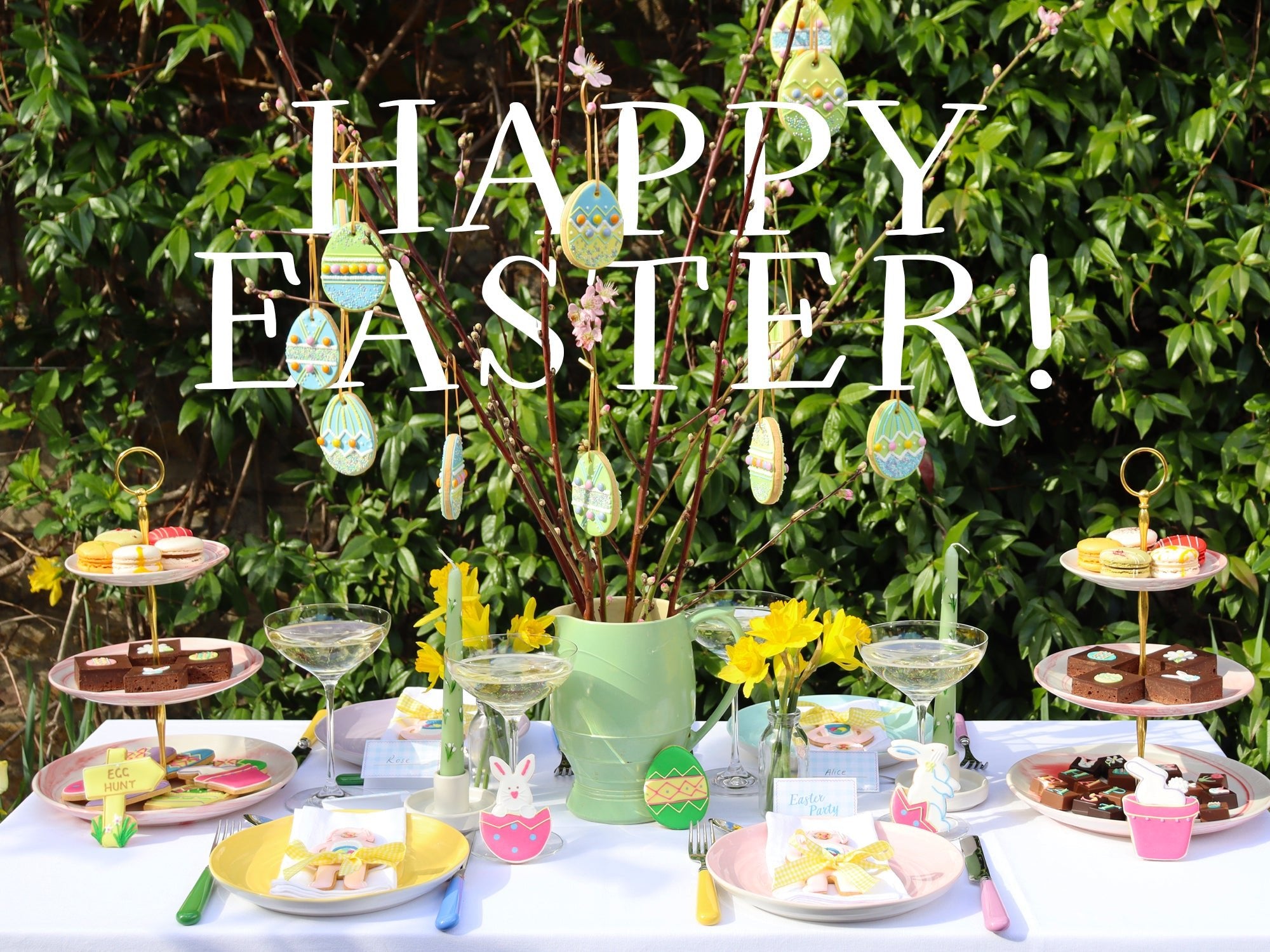 Easter table with DIY Easter Tree, iced biscuits, and bunny ear napkins by Biscuiteers for spring celebrations and personalized gifts.